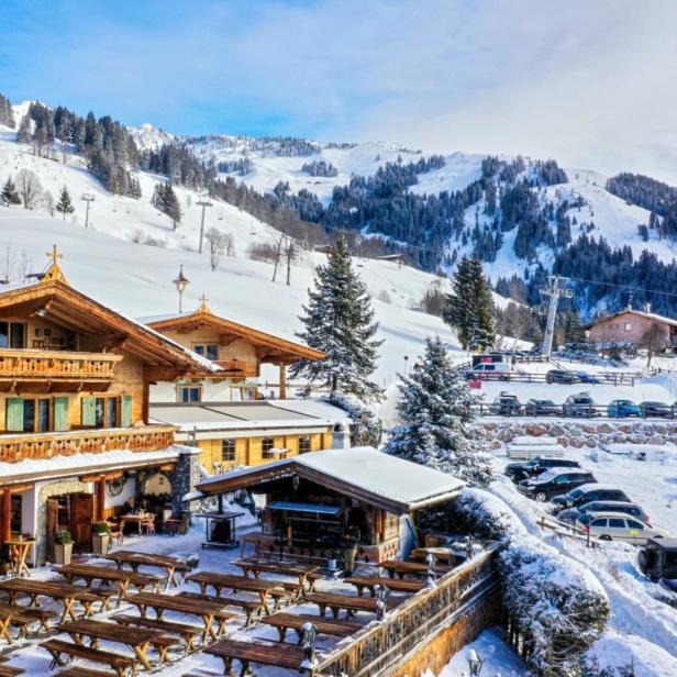 Ein Gasthof im Chalet-Stil vor einer verschneiten Berglandschaft mit Skipisten.