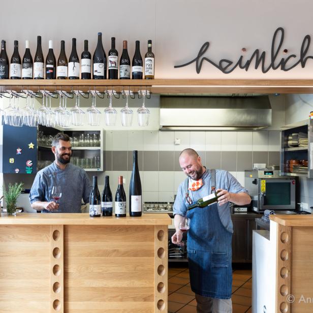 Zwei Männer stehen hinter einer Bar und schenken Wein in Gläser ein.