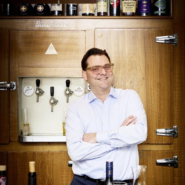 Ein Mann mit Brille steht vor einer Bar mit Getränken und Zapfhähnen.