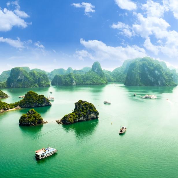 Boote fahren durch die Halong-Bucht in Vietnam, vorbei an bewaldeten Kalksteininseln.