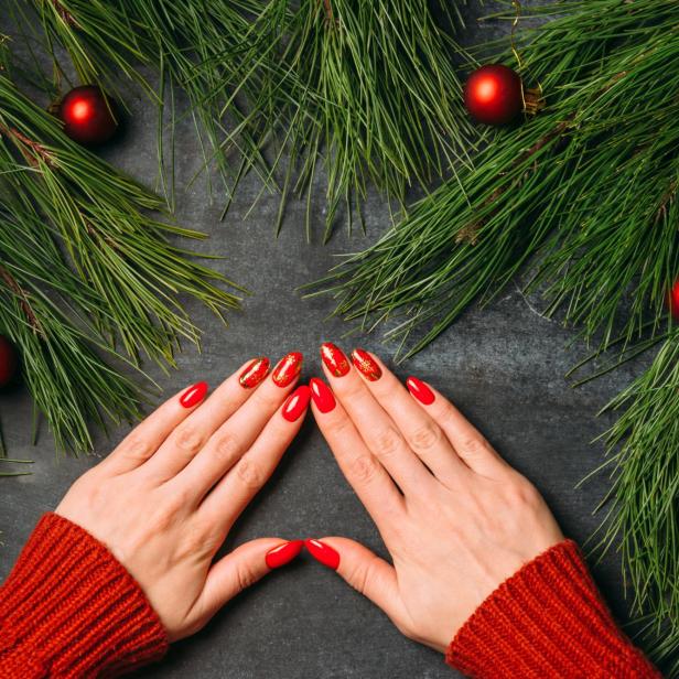 Hände mit rotem Nagellack und Weihnachtsmotiven vor Tannenzweigen und roten Kugeln.