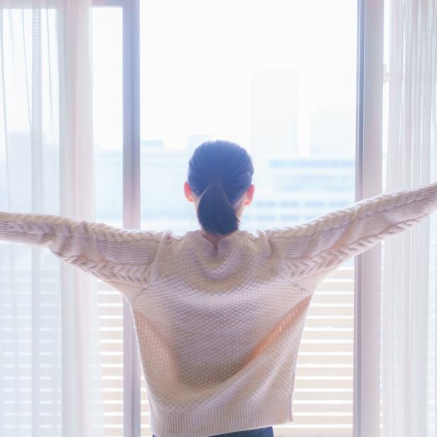 Eine Frau steht am Fenster und lüftet den Raum.