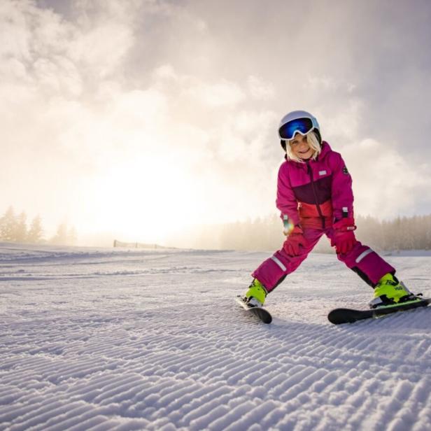 Ein Kind in Skikleidung steht auf einer Skipiste.