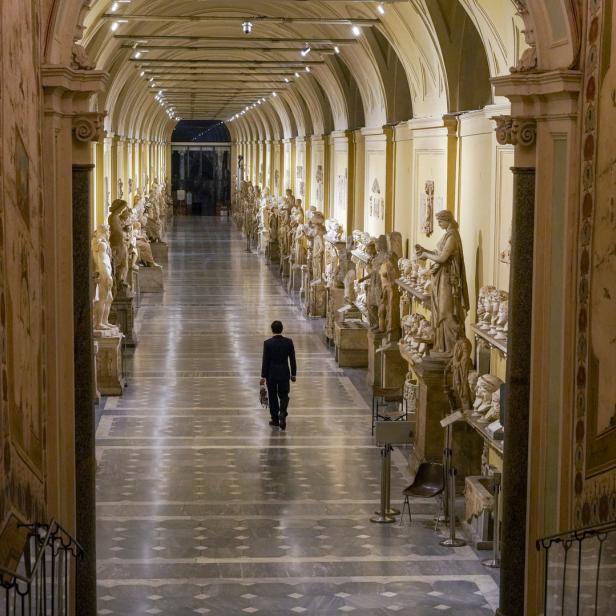Ein Mann geht durch einen langen Korridor, gesäumt von Statuen in einem Museum.