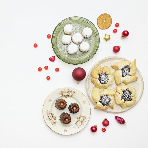 Verschiedene Weihnachtsplätzchen und rote Zuckerstreusel sind auf Tellern angerichtet.