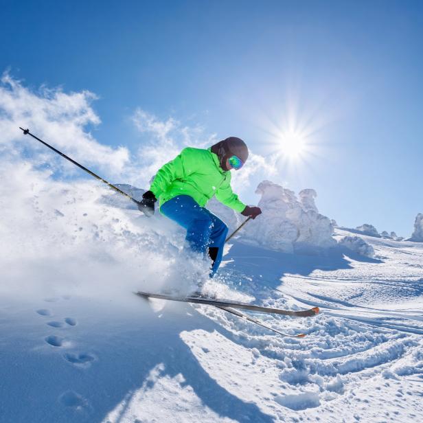 Ein Skifahrer fährt an einem sonnigen Tag einen schneebedeckten Hang hinunter.