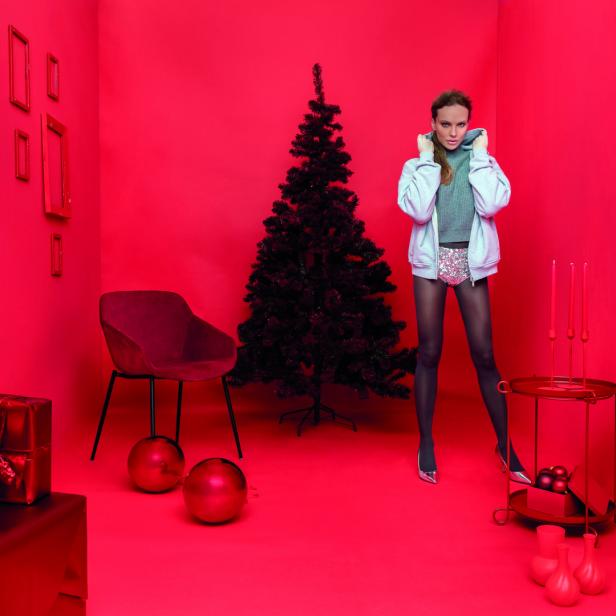 Eine Frau posiert in einem roten Raum mit Weihnachtsbaum und Geschenken.