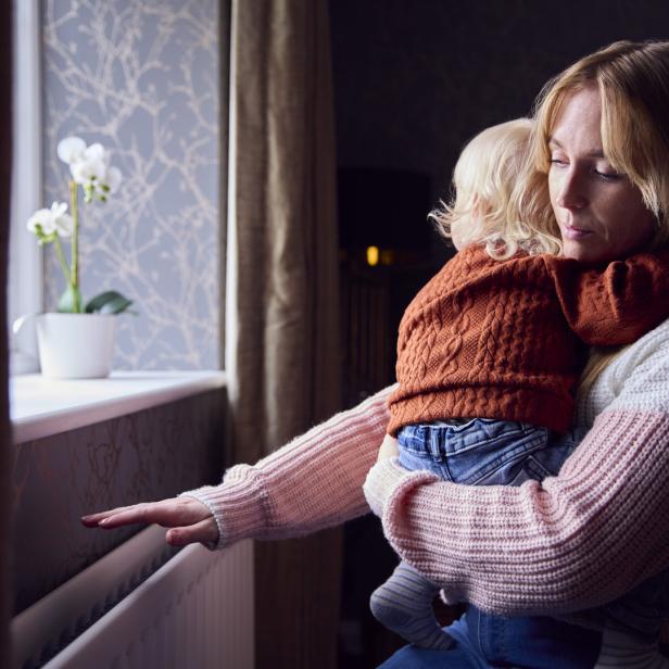 Eine Mutter hält ihr Kind am Fenster und berührt die Heizung.