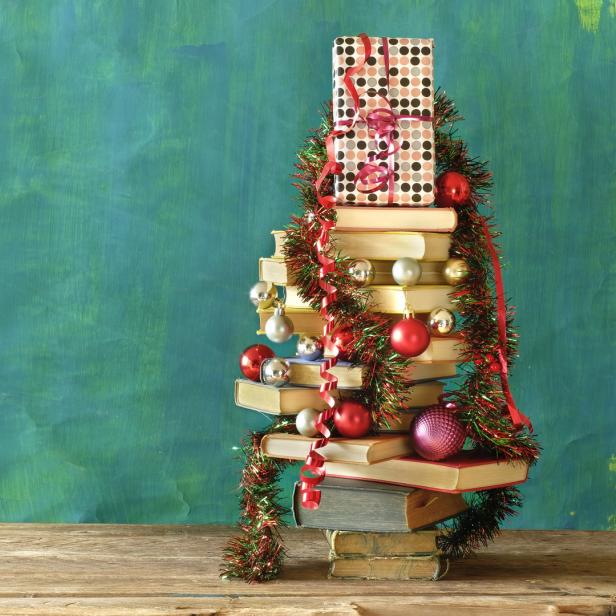 Ein Bücherstapel ist als Weihnachtsbaum mit Geschenk, Kugeln und Girlande geschmückt.