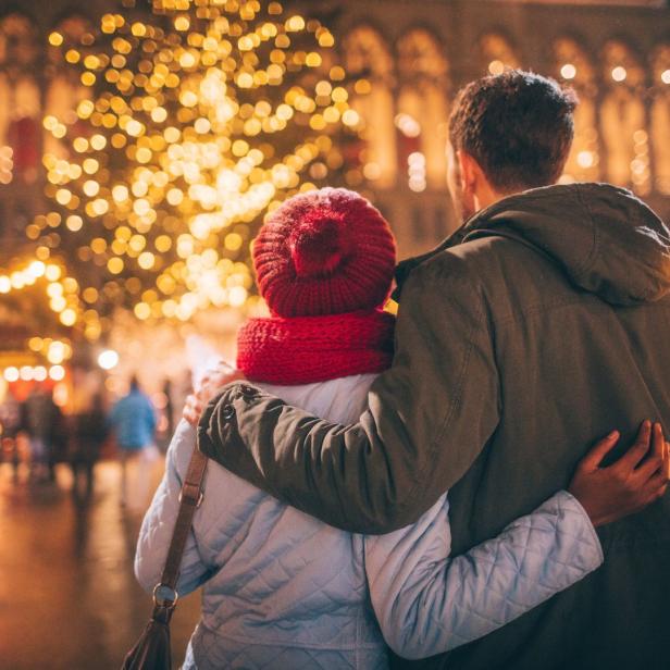 Ein Paar umarmt sich vor einem Weihnachtsbaum auf einem Weihnachtsmarkt.