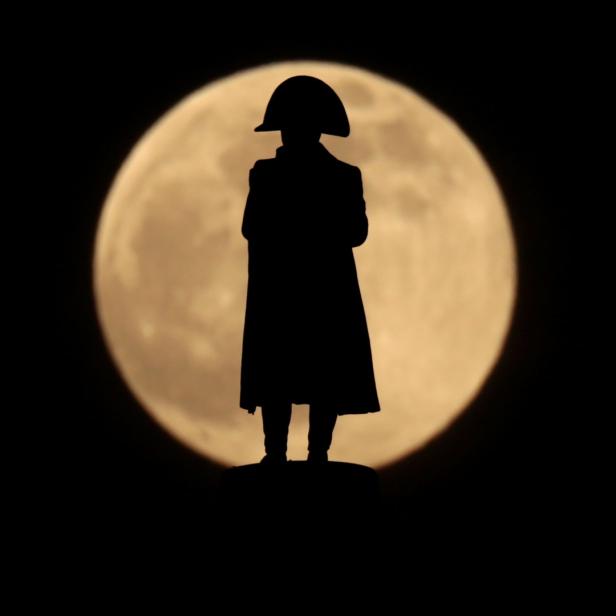 Die Silhouette einer Napoleon-Statue vor einem Vollmond.