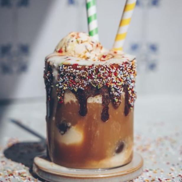 Ein Milchshake mit Eis, Schokosauce und bunten Streuseln, garniert mit zwei Strohhalmen.