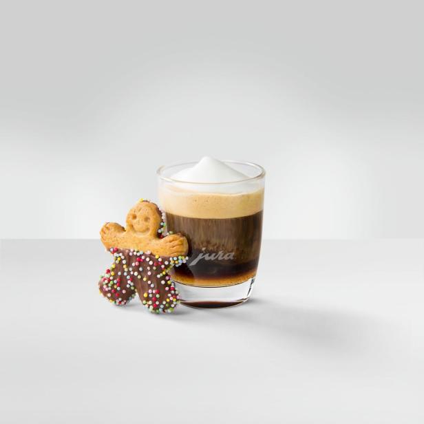 Ein Lebkuchenmann steht neben einem Glas Kaffee mit Milchschaum.