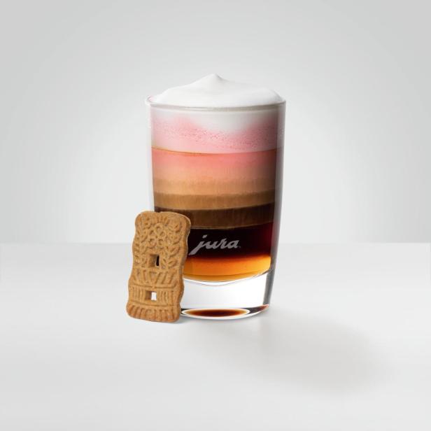 Ein Glas Latte Macchiato mit einem Keks der Marke Jura daneben.