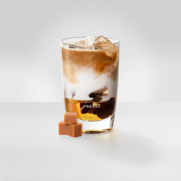 Ein Glas mit Eiskaffee und Karamellwürfeln auf einem Tisch.