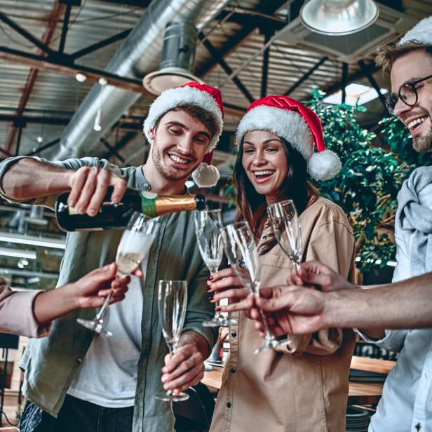 Eine Gruppe von Freunden mit Weihnachtsmützen stößt mit Sektgläsern an.