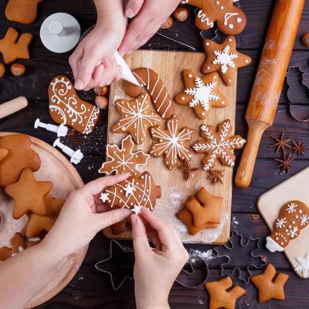 Hände verzieren Lebkuchen mit Zuckerguss auf einem Holztisch.