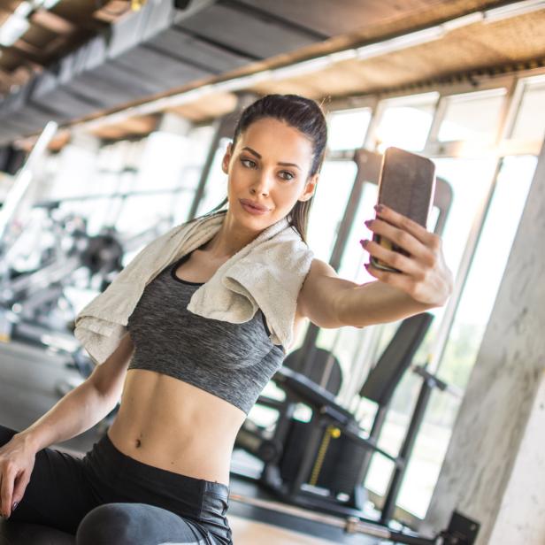 Eine Frau macht ein Selfie auf einem Gymnastikball in einem Fitnessstudio.