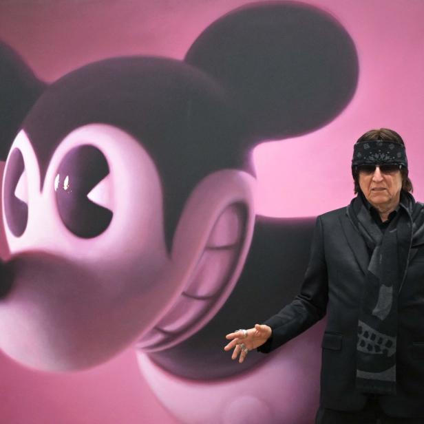 Ein Mann mit Sonnenbrille und Kopftuch posiert vor einem großen Mickey-Mouse-Gemälde.