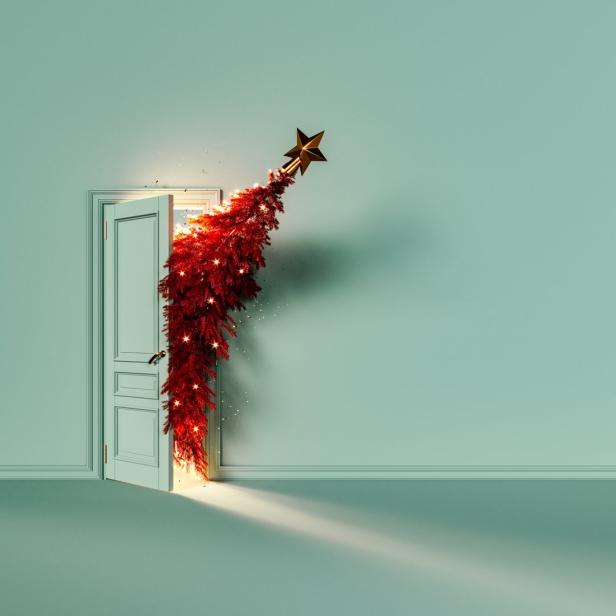 Ein rot geschmückter Weihnachtsbaum scheint aus einer offenen Tür in einem mintgrünen Raum zu wachsen.