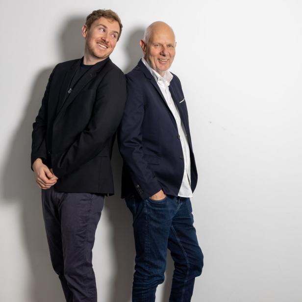 Matthias und Tristan Horx stehen Rücken an Rücken vor einer weißen Wand.