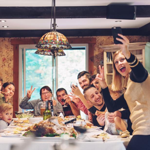 Eine Familie sitzt an einem Tisch mit Essen und macht ein Selfie.