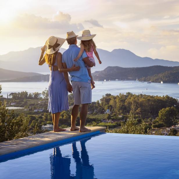 Eine Familie mit Kind genießt die Aussicht von einem Hotelpool auf das Meer.