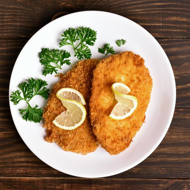 Zwei Wiener Schnitzel auf einem Teller mit Zitrone und Petersilie.