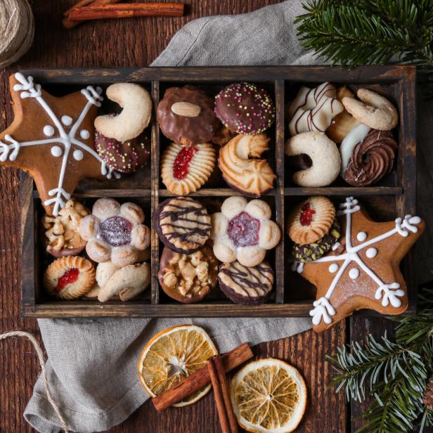 Weihnachtskekse in einer Holzkiste mit Tannenzweigen und Orangenscheiben.