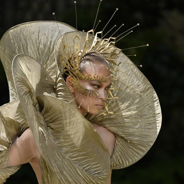 Ein Model präsentiert ein extravagantes goldenes Kleid und einen Kopfschmuck.