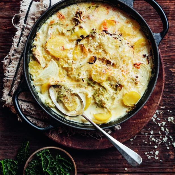 Ein Kartoffelgratin mit Grünkohl in einer schwarzen Pfanne auf einem Holztisch.