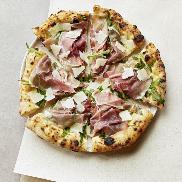 Eine Pizza mit Prosciutto, Rucola und Käse liegt auf einem Teller.