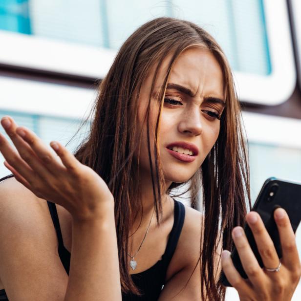 Eine junge Frau blickt irritiert auf ihr Smartphone.