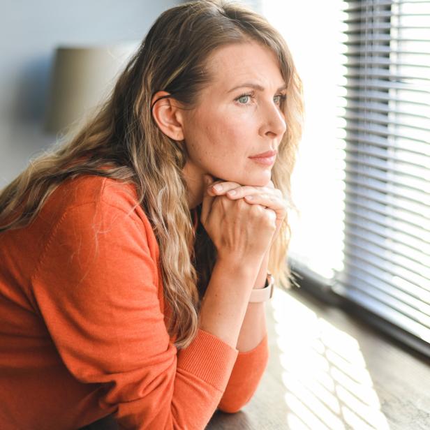 Frau schaut nachdenklich aus dem Fenster.