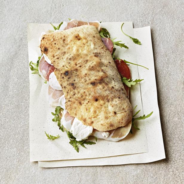 Ein Panuozzo Napoletano mit Mozzarella, Schinken und Rucola auf Papier serviert.