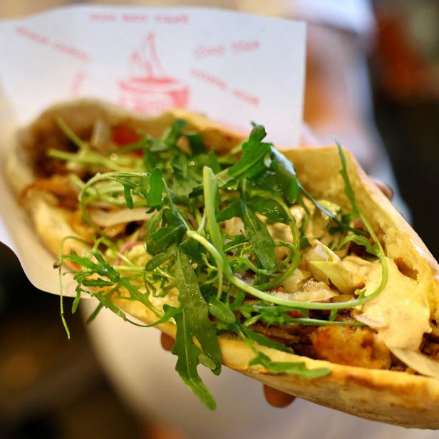 Ein Döner Kebap mit Salat und Soße wird in der Hand gehalten.