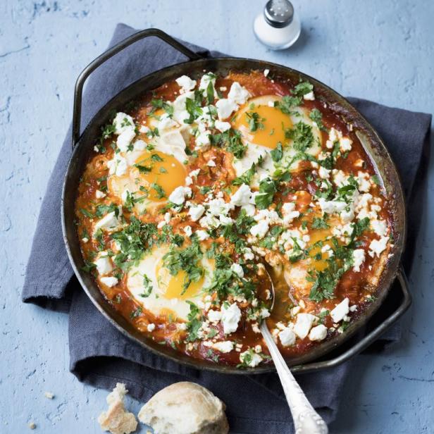 Shakshuka mit Eiern, Tomaten, Feta und Petersilie in einer Pfanne serviert.