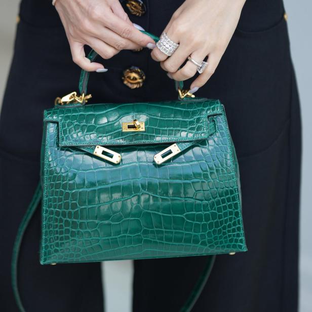 Eine Frau hält eine grüne Krokodillederhandtasche mit goldenen Akzenten.