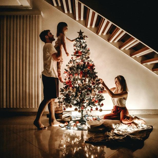 Eine Familie schmückt gemeinsam einen Weihnachtsbaum im Wohnzimmer.