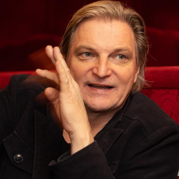 Porträt des Schauspielers Burghart Klaußner vor einem roten Hintergrund.
