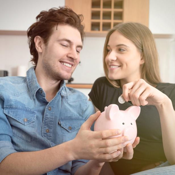 Ein Paar füttert gemeinsam ein rosa Sparschwein mit Münzen.