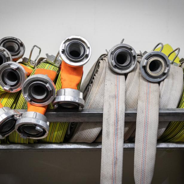 Mehrere zusammengerollte Feuerwehrschläuche liegen in einem Regal.