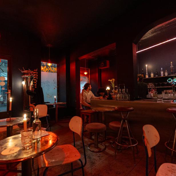 Innenansicht einer Bar mit gedämpftem, rotem Licht und Gästen.