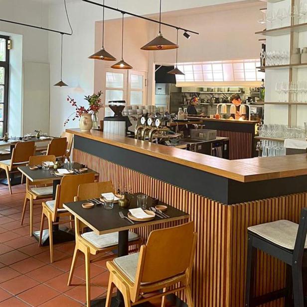Innenansicht eines Restaurants mit Tischen, Stühlen und einer Bar.
