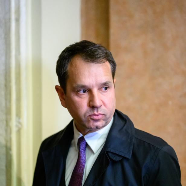 Ein Mann mit dunklem Haar und Mantel blickt zur Seite.