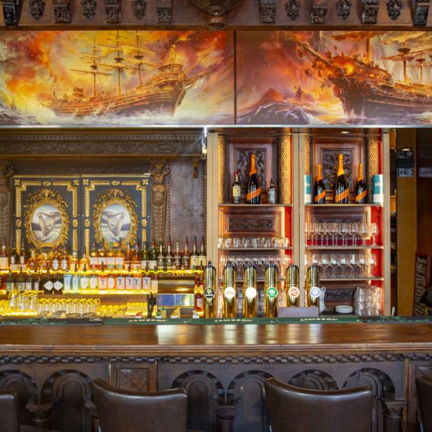 Eine Bar mit einer großen Auswahl an Spirituosen und einem Gemälde von Schiffen in stürmischer See.