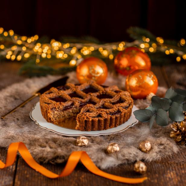 Eine gedeckte Linzertorte mit Weihnachtsschmuck auf einem Holztisch.