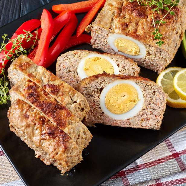 Ein Hackbraten mit gekochten Eiern, Paprika, Zitrone und Avocado auf einem Teller.