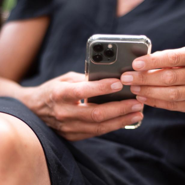 Person hält ein schwarzes Handy in den Händen.