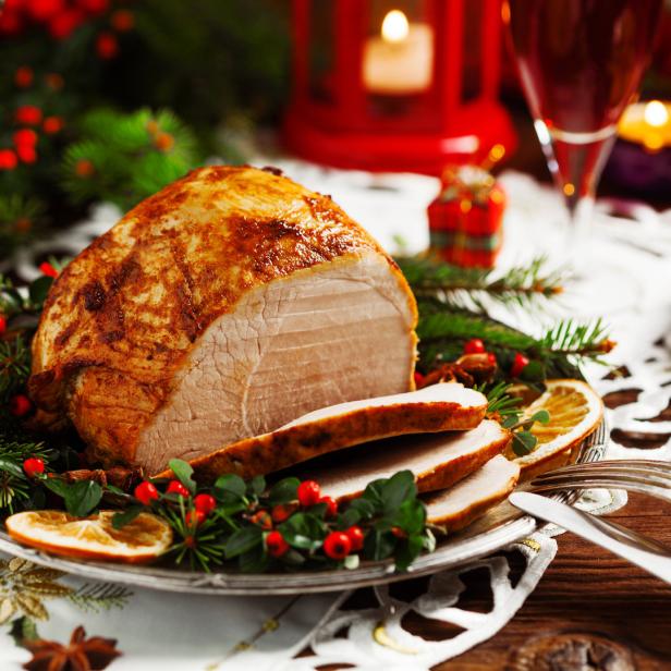 Ein festlicher Braten, garniert mit Beeren und Orangenscheiben, auf einem Tisch mit Weihnachtsdekoration.